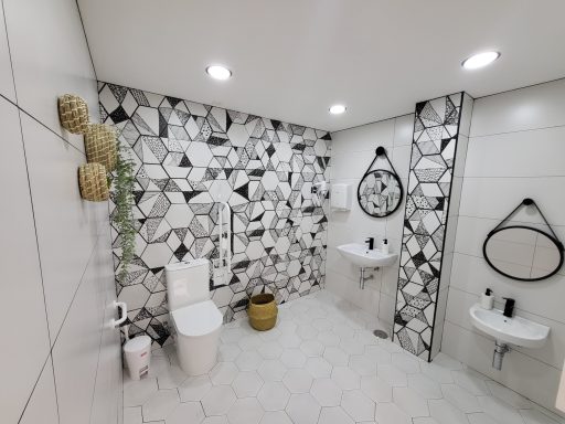 Baño moderno con azulejos en blanco y negro, inodoro, lavabo y espejos redondos.