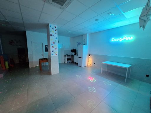 Sala iluminada con luces de colores y decoración sencilla, con mesas y una zona de juegos.