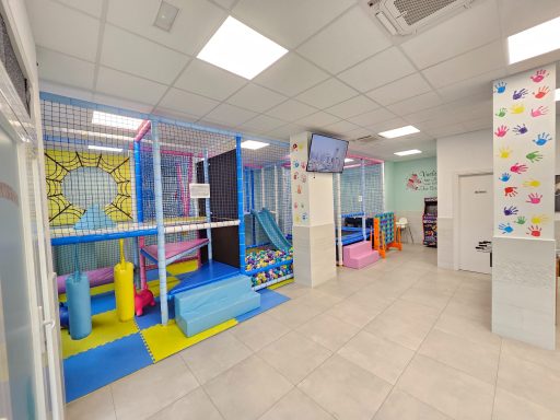 Zona de juegos infantil colorida con estructuras de escalada y colchonetas en un espacio amplio.